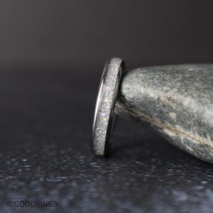 side profile of thin moonstone ring showing polished edges and sparkling crushed inlay on dark textured surface
