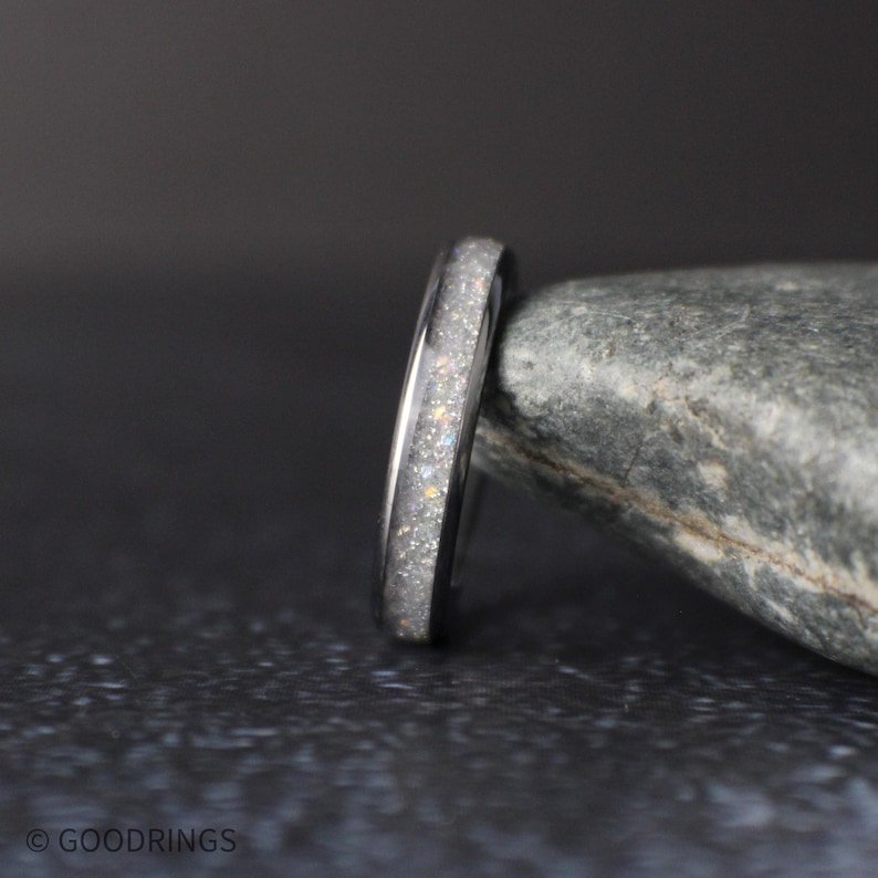 side profile of thin moonstone ring showing polished edges and sparkling crushed inlay on dark textured surface