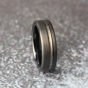 May include: A black tungsten carbide ring with a brushed finish and a silver inlay. The ring is a classic style and would make a great wedding band.
