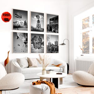 Peut inclure: Un ensemble de six photographies en noir et blanc encadrées, représentant diverses scènes : un panneau de motel, un moulin à vent, un bâtiment avec balcon, des montgolfières, des personnages et une église. Elles sont accrochées au-dessus d'un canapé blanc.