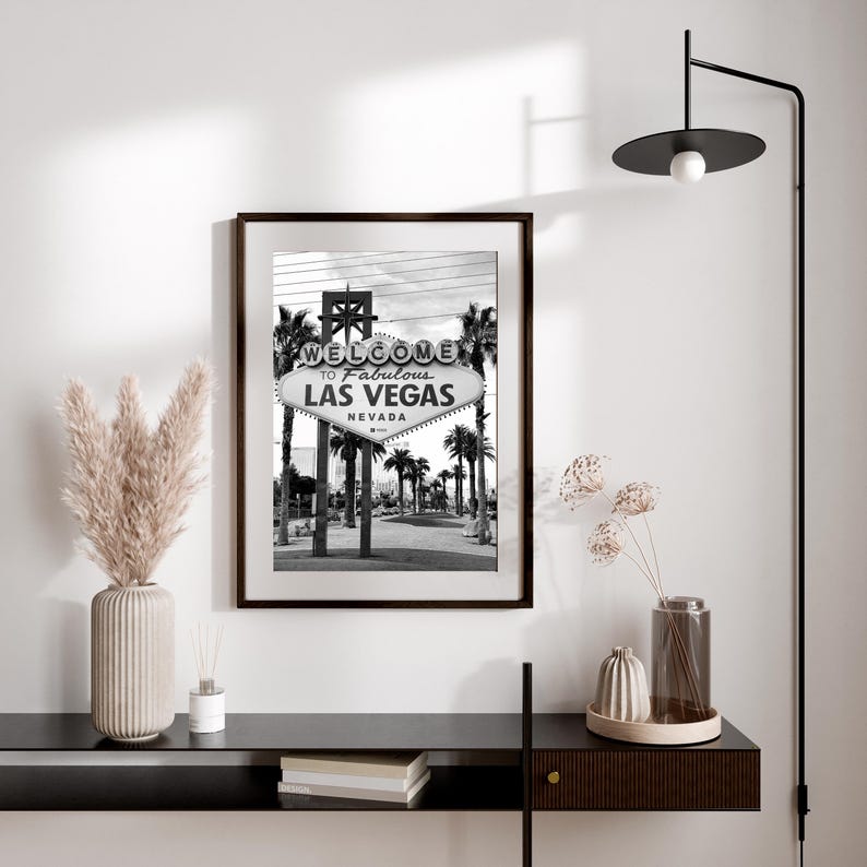 May include: Black and white framed print of the iconic "Welcome to Fabulous Las Vegas" sign, with palm trees in the background. The sign is centered in the image, with the text "Las Vegas Nevada". The print is displayed on a white wall.