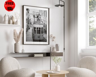 May include: Black and white photograph of a vintage tram traveling up a hill in a city. The photo is framed and hanging on a white wall above a shelf with decorative items.