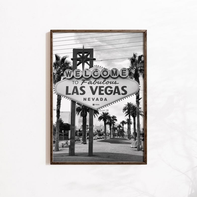 May include: Black and white framed print of the iconic "Welcome to Fabulous Las Vegas Nevada" sign. The sign is oval-shaped with a starburst design at the top and is surrounded by palm trees. The image is a classic representation of Las Vegas.