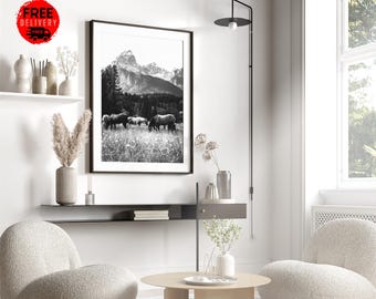 May include: Black and white photograph of a mountain range with a herd of elk grazing in a field. The photo is framed and hanging on a white wall in a living room setting.