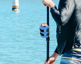 May include: A blue and black paddleboard cup holder with a can of soda inside. The holder is attached to a paddle.
