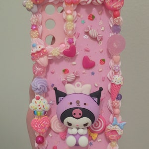 May include: A pink phone case decorated with a purple and black Kuromi character, candy, hearts, and sprinkles. The case has a raised 3D design and is made of resin.