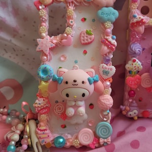 May include: A pink and white phone case decorated with a cartoon character, candy, and hearts. The case has the words "Angel-e" and "Love" on it.