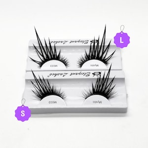 May include: Two pairs of black false eyelashes with a spiky design. The eyelashes are packaged in a white plastic case with the brand name "Elegant Lashes" printed on it. The case has two compartments, each containing a pair of eyelashes. The eyelashes are labelled "Mystic" and "MO33". The image also shows two tags, one labelled "S" and the other labelled "L".