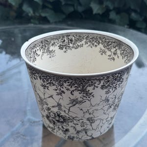 Könnte beinhalten: Ein weißer Keramiktopf mit einem schwarz-weißen Blumenmuster. Der Topf ist rund und hat einen breiten Rand.