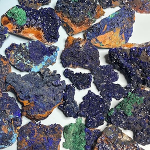 Puede incluir: Una colección de especímenes minerales de azurita en bruto. Las piedras muestran un color azul profundo con parches verdes y naranjas. La textura rugosa y las formaciones naturales son visibles.