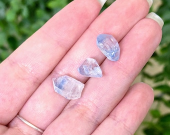 May include: Three small, translucent, light blue crystal points with jagged, natural edges and internal inclusions. These raw, pale blue mineral specimens are faceted by nature, displaying varying shapes and sizes with a clear, icy appearance.