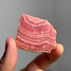 May include: A pink and white banded mineral specimen with a layered, striated texture. The mineral is translucent and has a smooth, polished surface.