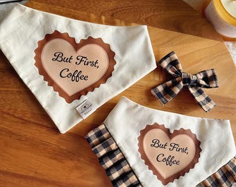 Op de afbeelding: Twee crèmekleurige huisdierbandana's en een bijpassende strik. Elke bandana heeft een bruine hartvormige afbeelding met de tekst "But First, Coffee" in zwarte letters. Eén bandana heeft een geplooide zwart-bruine ruitjesrand.