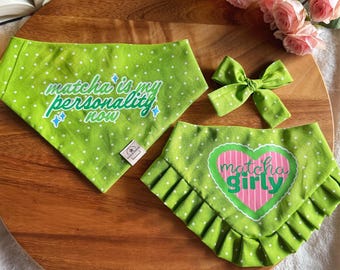 Puede incluir: Dos pañuelos para mascotas de color verde lima con lunares blancos, uno con el texto "matcha is my personality now" y el otro con un corazón rosa y el texto "matcha girly", además de un lazo verde a juego.