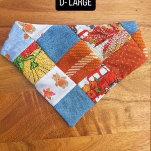 Puede incluir: Un pa&ntilde;uelo triangular para mascotas con dise&ntilde;o de parches que combina tela azul tipo mezclilla, cuadrados naranjas texturizados y paneles blancos estampados con ositos, calabazas, camiones rojos y hojas de oto&ntilde;o. Texto D-LARGE visible.