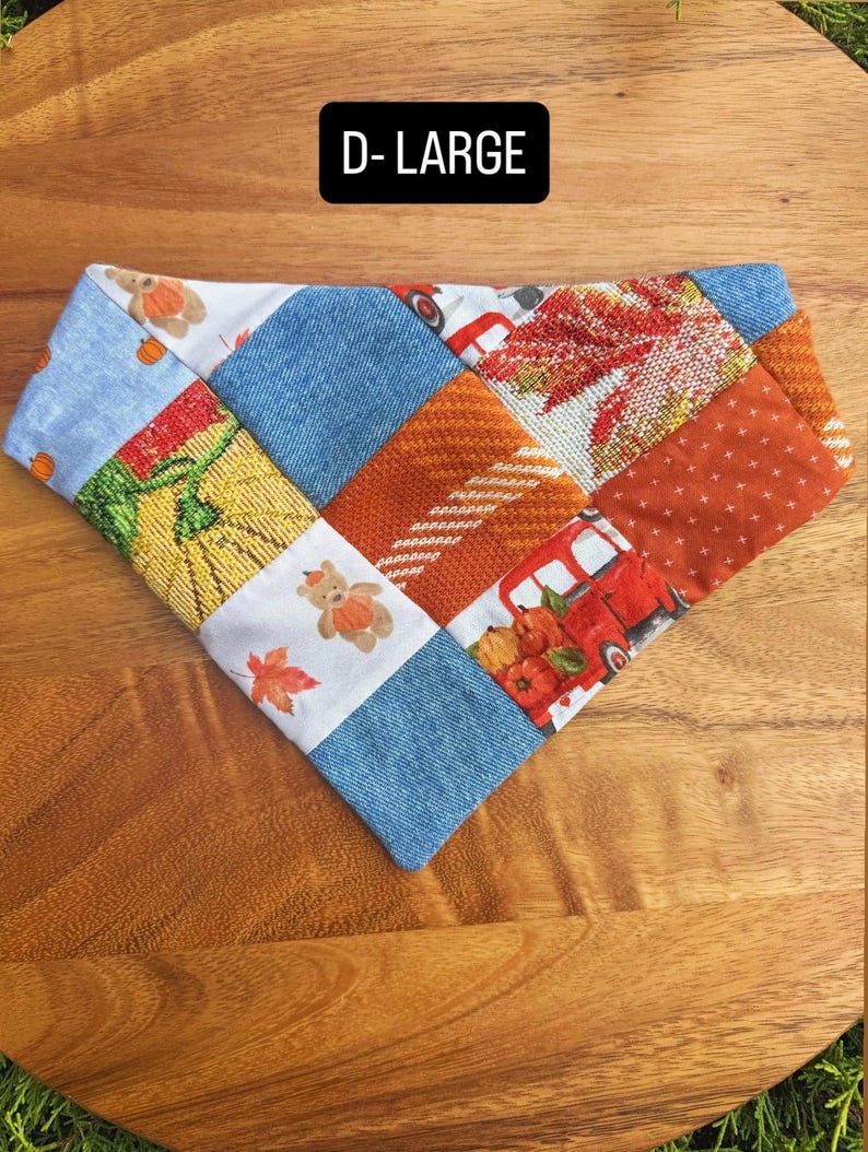 Puede incluir: Un pa&ntilde;uelo triangular para mascotas con dise&ntilde;o de parches que combina tela azul tipo mezclilla, cuadrados naranjas texturizados y paneles blancos estampados con ositos, calabazas, camiones rojos y hojas de oto&ntilde;o. Texto D-LARGE visible.