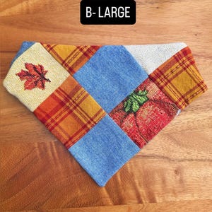 Puede incluir: Un pa&ntilde;uelo triangular para mascota con dise&ntilde;o de parches en mezclilla azul, cuadros naranjas y amarillos, y tela crema con un estampado de hoja de arce roja y una calabaza. El texto B-LARGE est&aacute; impreso en blanco sobre un fondo negro.