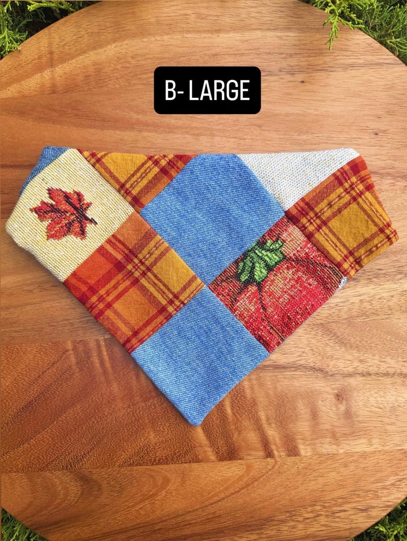 Puede incluir: Un pa&ntilde;uelo triangular para mascota con dise&ntilde;o de parches en mezclilla azul, cuadros naranjas y amarillos, y tela crema con un estampado de hoja de arce roja y una calabaza. El texto B-LARGE est&aacute; impreso en blanco sobre un fondo negro.