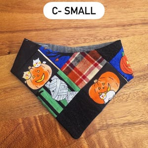 May include: A triangular pet bandana featuring a patchwork design with Halloween motifs including orange pumpkins, white cats, and a mummy. The fabric includes black, green, blue, and red plaid sections. The text C- SMALL is printed above the item.