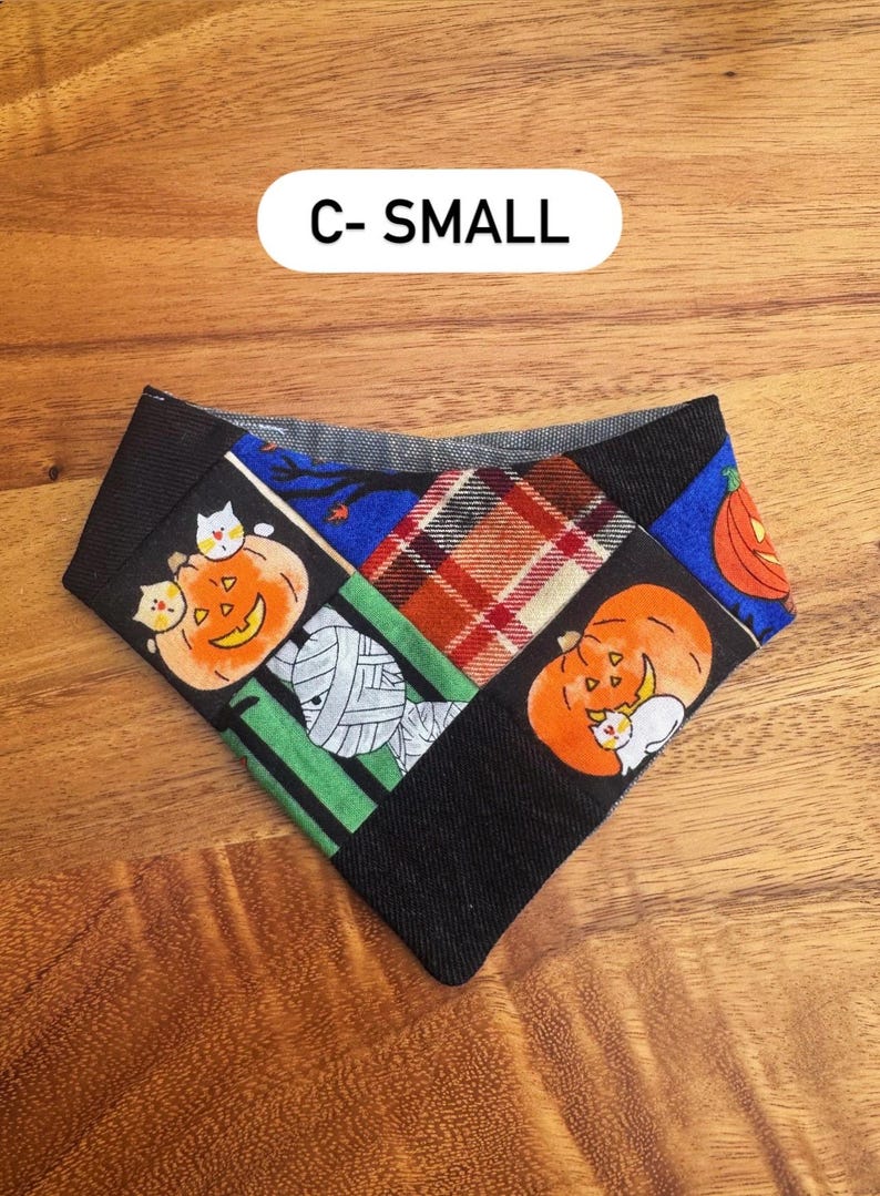 May include: A triangular pet bandana featuring a patchwork design with Halloween motifs including orange pumpkins, white cats, and a mummy. The fabric includes black, green, blue, and red plaid sections. The text C- SMALL is printed above the item.