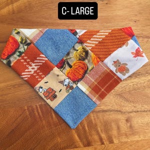 Puede incluir: Un pa&ntilde;uelo triangular para mascotas con un dise&ntilde;o de patchwork de telas con tem&aacute;tica oto&ntilde;al, que incluye calabazas naranjas, cuadros, tela azul efecto mezclilla y un estampado de Snoopy. El texto C-LARGE est&aacute; impreso en blanco.