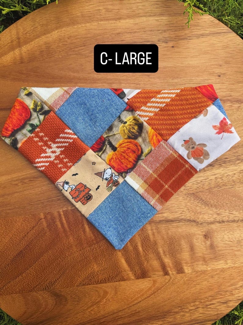 Puede incluir: Un pa&ntilde;uelo triangular para mascotas con un dise&ntilde;o de patchwork de telas con tem&aacute;tica oto&ntilde;al, que incluye calabazas naranjas, cuadros, tela azul efecto mezclilla y un estampado de Snoopy. El texto C-LARGE est&aacute; impreso en blanco.