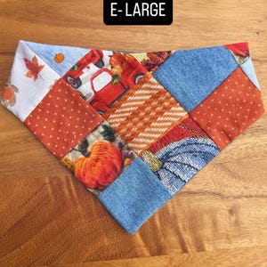 Puede incluir: Un pa&ntilde;uelo triangular para mascotas con un dise&ntilde;o de retazos de varias telas, incluyendo estampados de calabazas naranjas, ilustraciones de camiones rojos, texturas tipo mezclilla azul y hojas de oto&ntilde;o. El texto E-LARGE est&aacute; en blanco.