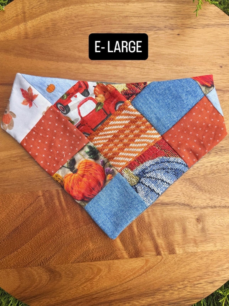 Puede incluir: Un pa&ntilde;uelo triangular para mascotas con un dise&ntilde;o de retazos de varias telas, incluyendo estampados de calabazas naranjas, ilustraciones de camiones rojos, texturas tipo mezclilla azul y hojas de oto&ntilde;o. El texto E-LARGE est&aacute; en blanco.