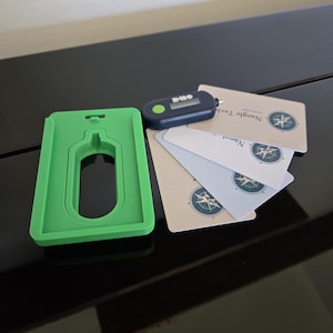 May include: A green plastic card holder, a small black and blue digital device, and several white cards with a compass rose design and the text "Nangle Tech". The items are arranged on a glossy black surface.