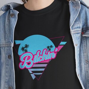 May include: Black t-shirt with a retro-style graphic design featuring a blue circle with palm trees, a pink and blue triangle, and the text "Bitchin'" in pink and blue letters.