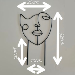 Puede incluir: Escultura de alambre de metal negro de una cara estilizada. La escultura tiene 20 cm de ancho, 32 cm de alto y 14 cm de profundidad. La escultura est&aacute; sobre un fondo blanco.