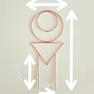 Puede incluir: Una decoraci&oacute;n de pared geom&eacute;trica de metal de color cobre con un c&iacute;rculo, un tri&aacute;ngulo y dos l&iacute;neas verticales. La decoraci&oacute;n mide 20 cm de ancho, 47 cm de alto y 10 cm de profundidad.