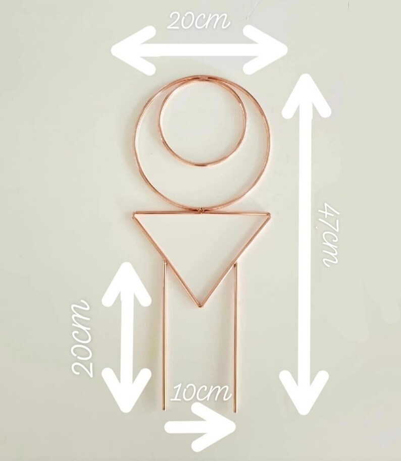 Puede incluir: Una decoraci&oacute;n de pared geom&eacute;trica de metal de color cobre con un c&iacute;rculo, un tri&aacute;ngulo y dos l&iacute;neas verticales. La decoraci&oacute;n mide 20 cm de ancho, 47 cm de alto y 10 cm de profundidad.