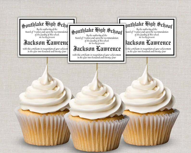 May include: Three cupcakes with white frosting and diploma toppers. The toppers read "Southlake High School" and "Jackson Lawrence" with the year 2024. The cupcakes are in paper liners.