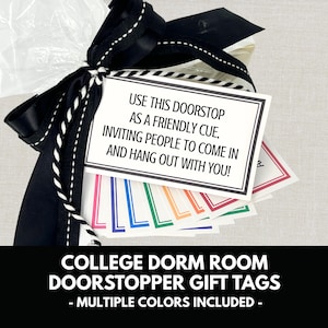 May include: A gift set featuring a black bow with white stitching, tied around a clear bag. The bag contains colorful doorstop gift tags. The tags have text that reads, "USE THIS DOORSTOP AS A FRIENDLY CUE, INVITING PEOPLE TO COME IN AND HANG OUT WITH YOU!"