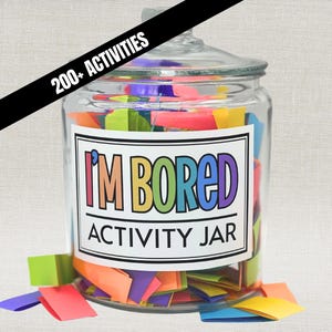 Op de afbeelding: Een doorzichtige glazen pot met deksel gevuld met kleurrijke papieren strookjes. Een wit etiket op de voorzijde bevat de tekst I'M BORED ACTIVITY JAR in veelkleurige letters. Een zwarte diagonale banner bovenaan toont 200+ ACTIVITIES.