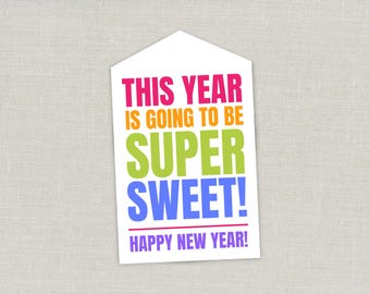 May include: A white rectangular tag with a pointed top featuring the colorful text THIS YEAR IS GOING TO BE SUPER SWEET! in pink, orange, green, and blue, followed by a horizontal pink line and the text HAPPY NEW YEAR! in purple lettering.