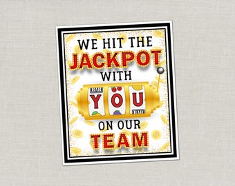 May include: A rectangular sign with a black border features the text "WE HIT THE JACKPOT WITH YOU ON OUR TEAM." The word "JACKPOT" is in red with gold trim. A gold slot machine graphic is in the center, with gold coins scattered around.