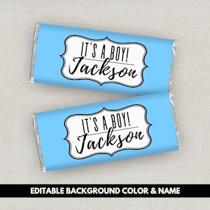 May include: Two rectangular candy bars wrapped in light blue paper. Each wrapper features a white scalloped label with a black border containing the black text IT'S A BOY! and the name Jackson in a cursive script font centred on the front.