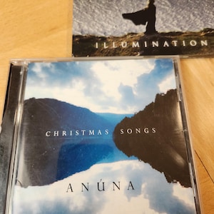 May include: Two CD cases are displayed. The top case is labeled "ANUNA" and "ILLUMINATION" with a silhouette of a person. The bottom case is labeled "CHRISTMAS SONGS" and "ANÚNA" with a landscape image.
