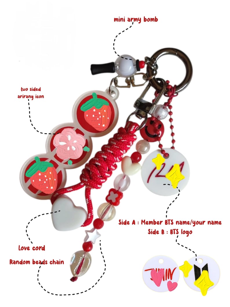 May include: A decorative keychain featuring a red braided cord, a white heart charm, and a random bead chain with red and clear beads. It includes a mini army bomb charm, a two-sided arirang icon with strawberry and flower designs, and a white circular tag.