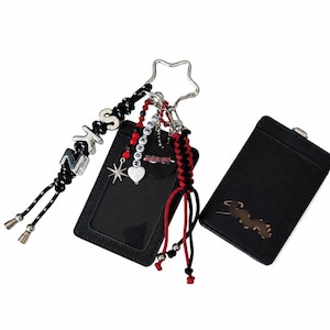 May include: Two black card holders with clear windows. One holder features a star-shaped keyring with black and red beaded charms, silver letter beads spelling SKZ and LEE KNOW, a heart charm, a star charm, and a red and black braided cord.