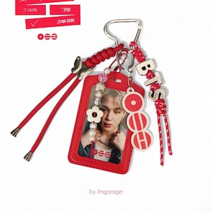 Könnte beinhalten: Roter Schlüsselanhänger mit einer Fotokarte. Der Schlüsselanhänger hat einen silbernen Verschluss, eine rote Kordel und dekorative Elemente wie eine Blume, Perlen und die Buchstaben "BTS". Der Text "BTS" und "by ilmgarae" sind sichtbar.