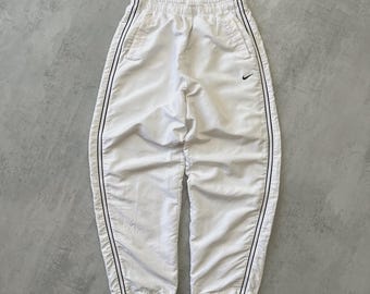 May include: White athletic pants with black stripes down the sides. The pants have a small black Nike logo on the left leg. The pants are made of a lightweight material and have an elastic waistband.