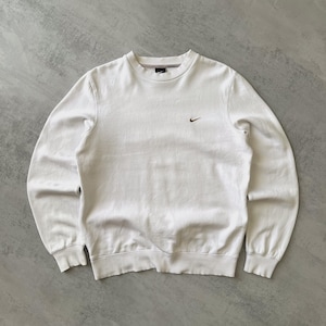 Puede incluir: Sudadera blanca de cuello redondo y manga larga. La sudadera presenta un peque&ntilde;o logotipo marr&oacute;n de Nike en la parte superior izquierda del pecho. Los pu&ntilde;os y el dobladillo son acanalados. El fondo es una superficie gris claro.