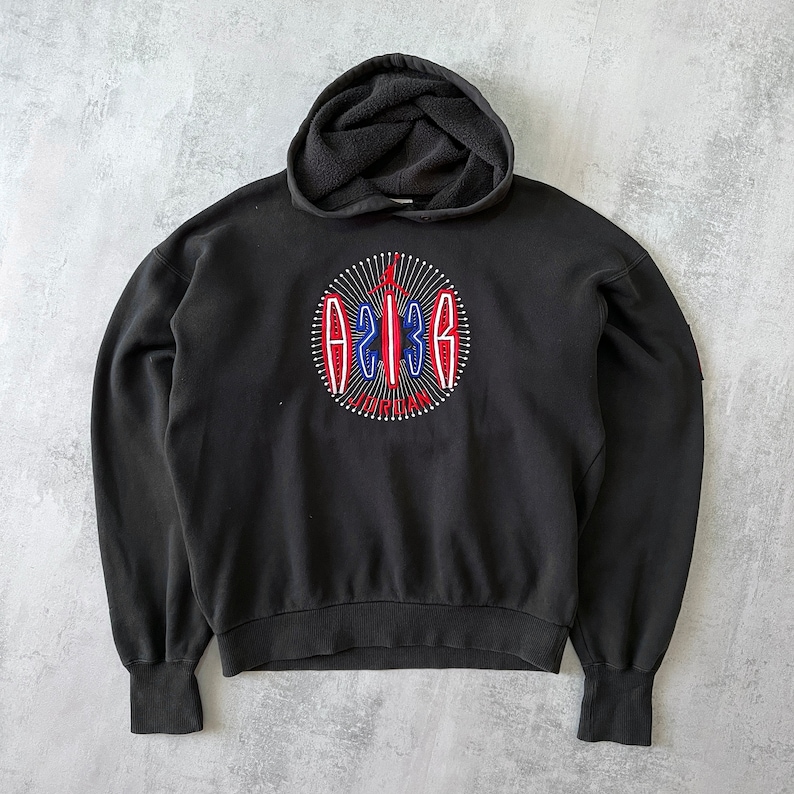 Puede incluir: Sudadera con capucha negra con un logotipo bordado en rojo, blanco y azul que dice "23" y "JORDAN".