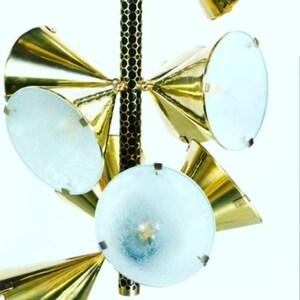 Puede incluir: Una lámpara de araña de vidrio esmerilado y dorado con una varilla central con estampado en blanco y negro. La lámpara de araña tiene seis luces y un diseño moderno.