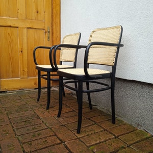 May include: Two black wooden chairs with woven cane seats. The chairs are in a brick patio area.