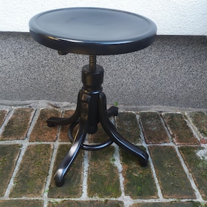 May include: A black adjustable stool with a round seat and a three-legged base. The seat is approximately 14 inches in diameter. The stool has a threaded central column for height adjustment.