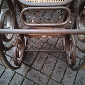 Peut inclure: Une chaise ber&ccedil;ante en bois brun avec un si&egrave;ge et un dossier en cannage. La chaise est pos&eacute;e sur un patio en briques.